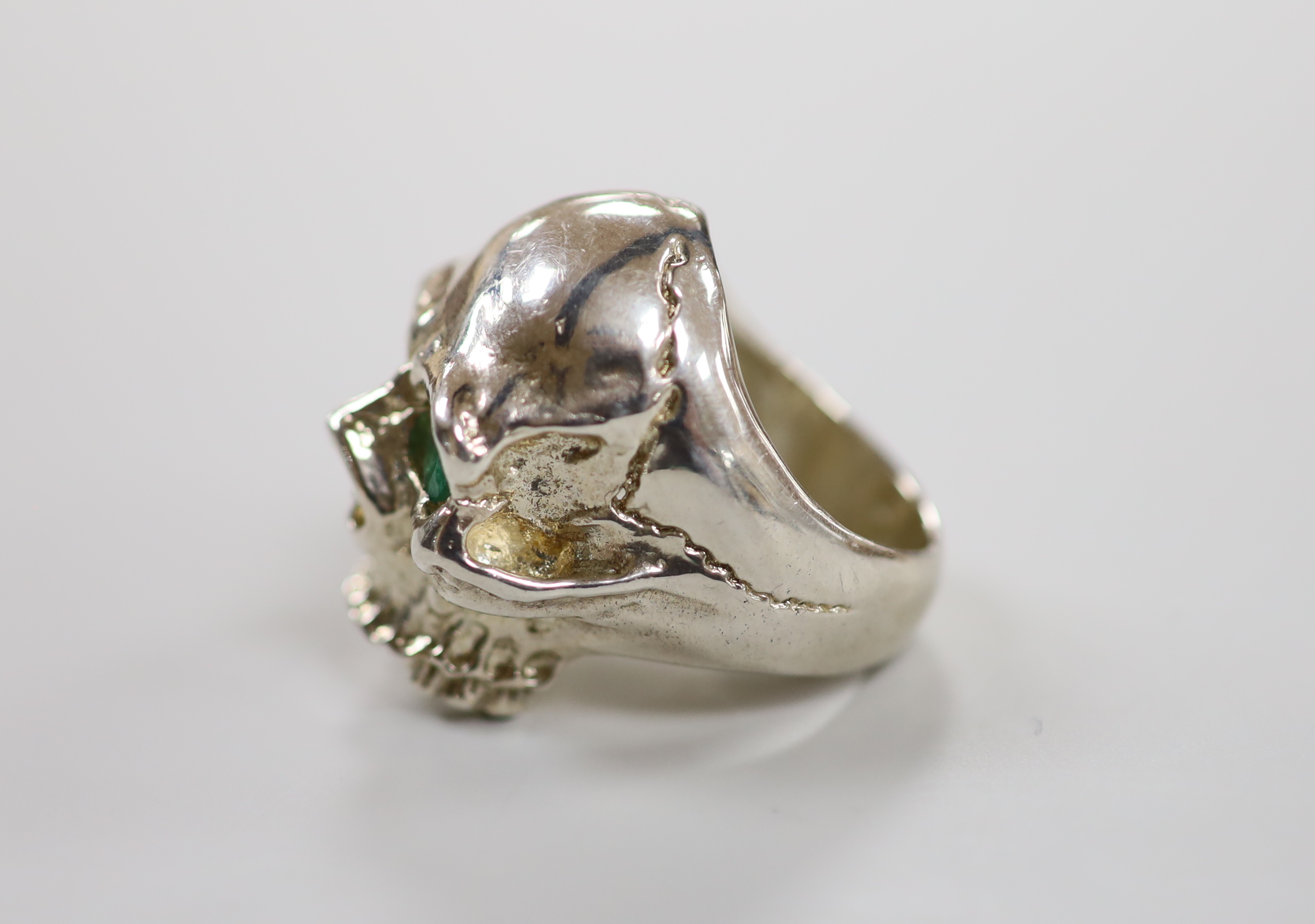 A white metal (tests a silver) and two stone emerald set skull ring, size T/U, gross weight 35,2 grams.